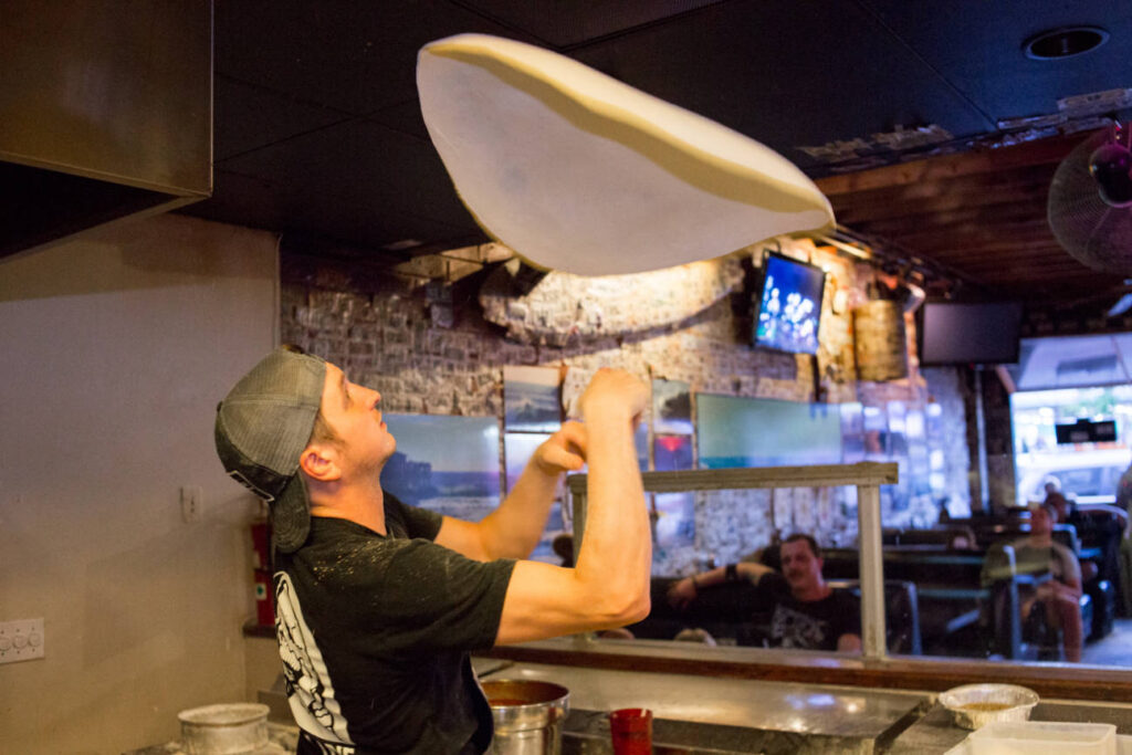 man flipping pizza dough